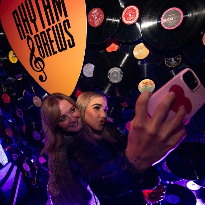 Rock band performing on stage with colorful lighting as attendees raise pints of craft beer